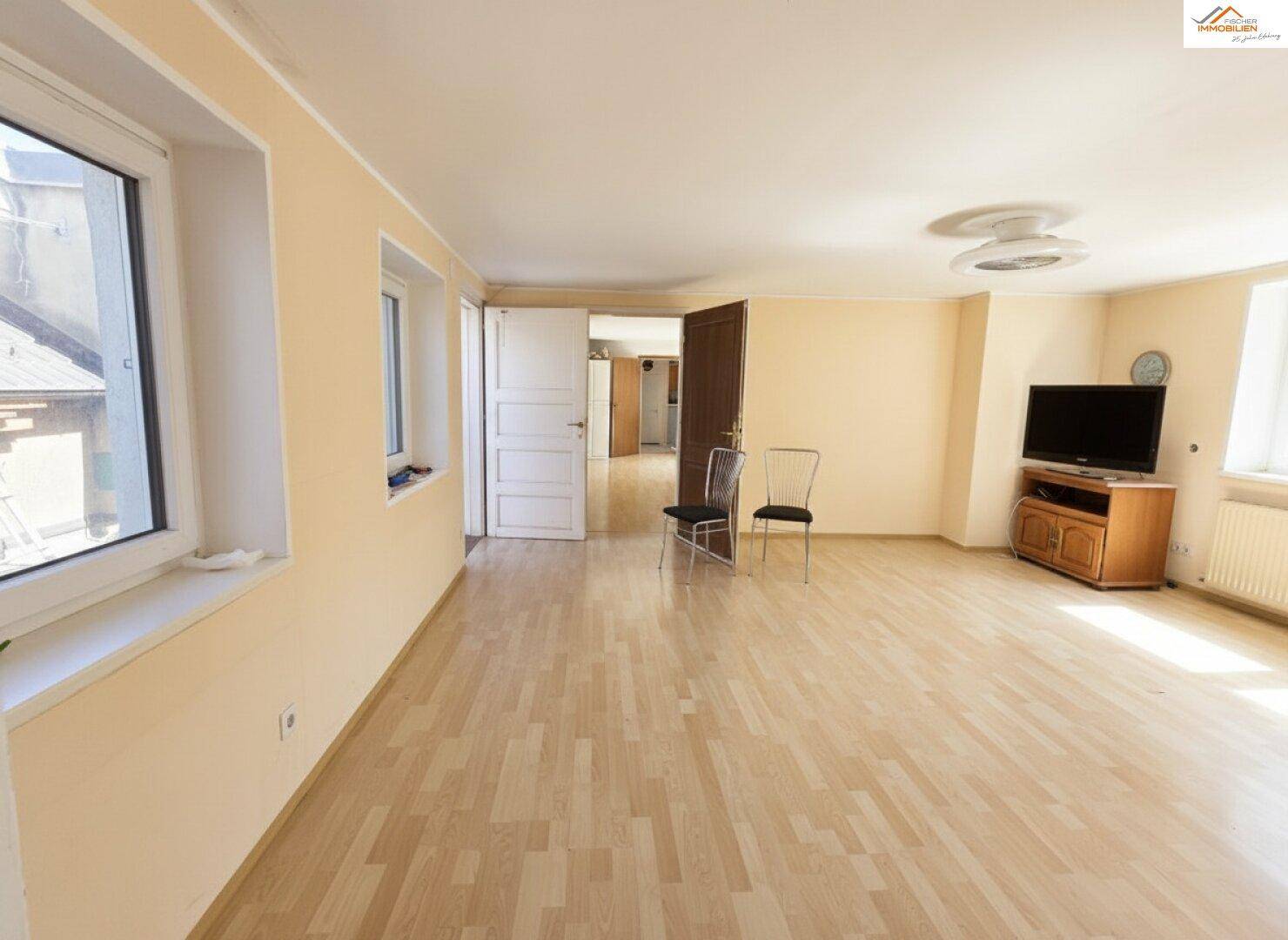 Großes Wohnzimmer mit Laminatboden, mehreren Fenstern und viel Tageslicht.
