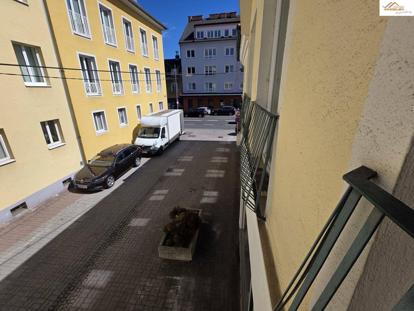 Blick von oben auf eine gepflasterte Straße mit parkenden Autos und umliegenden Gebäuden.
