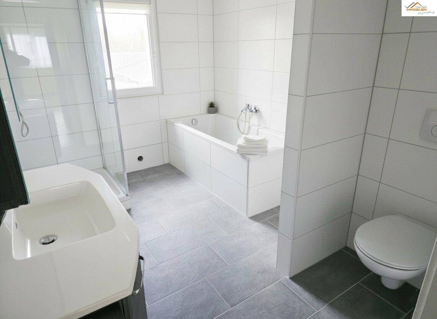 Modernes Badezimmer mit weißen Fliesen, Badewanne, Dusche und Fenster.