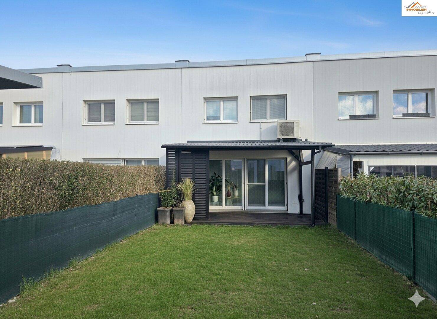 Hinterhof mit Rasenfläche, Hecke und überdachtem Terrassenbereich am Gebäude.