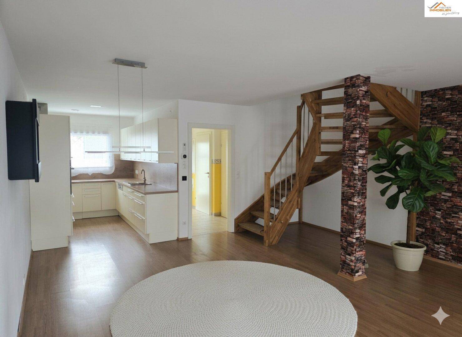 Offener Wohnbereich mit Holzboden, Treppe und integrierter Küche im Hintergrund.