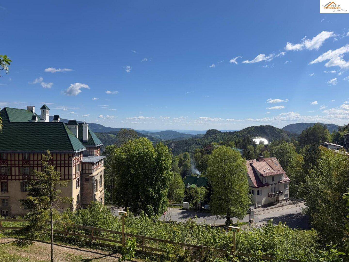 Weitläufiger Blick über die grüne Landschaft mit weiteren Gebäuden und Bergen am Horizont.