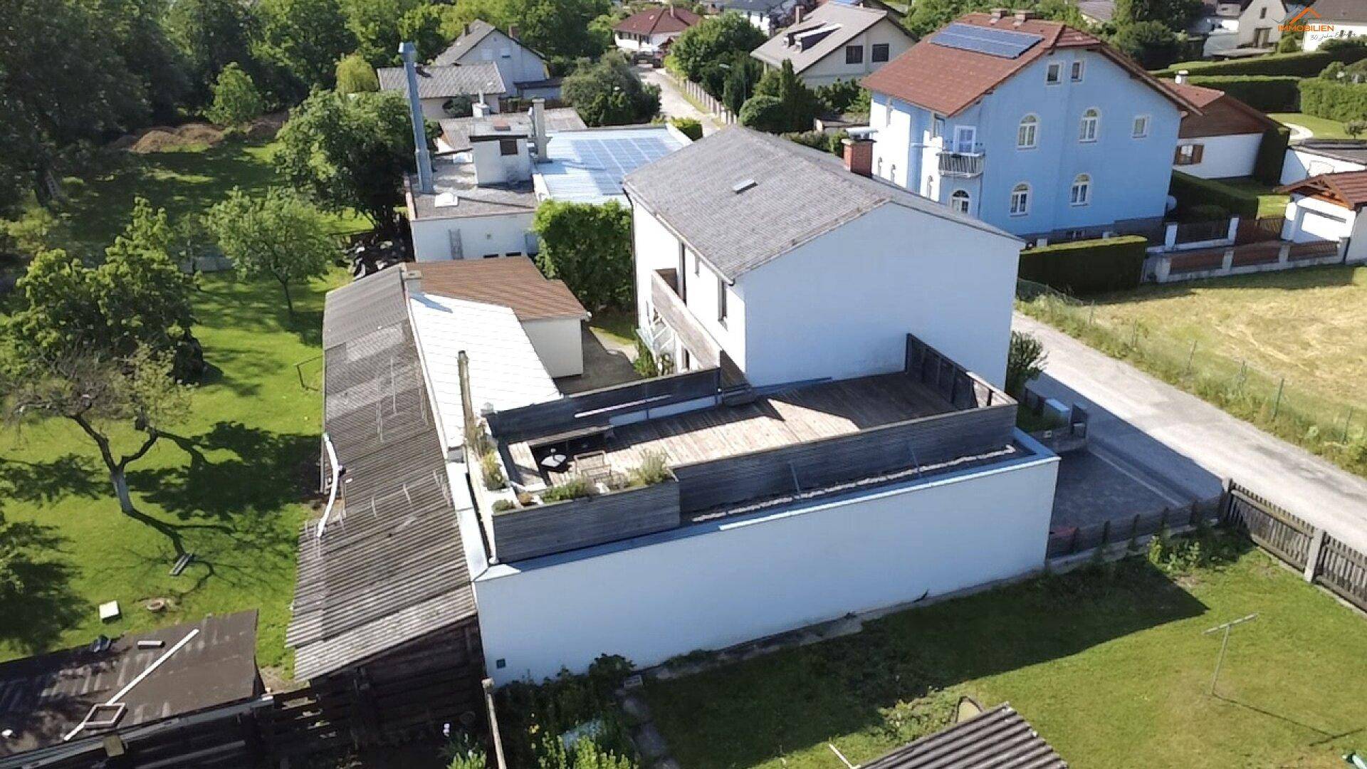 Rückansicht des Hauses mit einer großen Holzterrasse auf dem Flachdach und Blick auf die Umgebung.