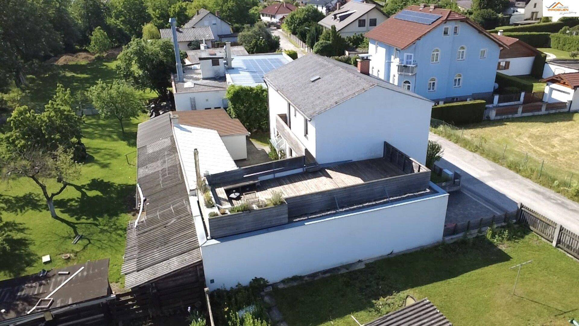 Rückansicht des Hauses mit großer Holzterrasse und Blick auf die umliegende Wohnbebauung und grüne Landschaft.