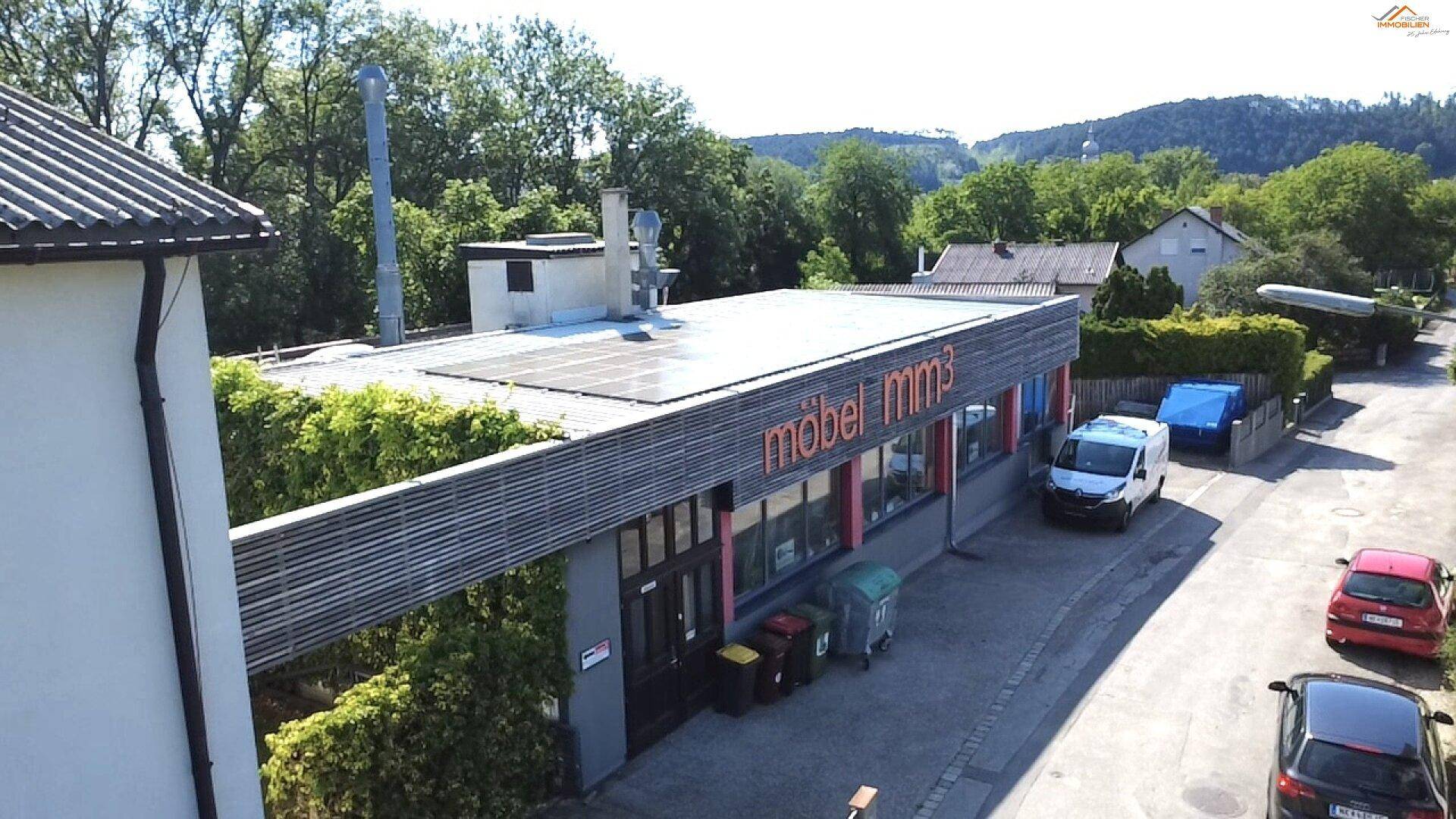 Luftaufnahme des Gewerbegebäudes "möbel mm3" mit Solaranlage auf dem Flachdach und parkenden Fahrzeugen davor.