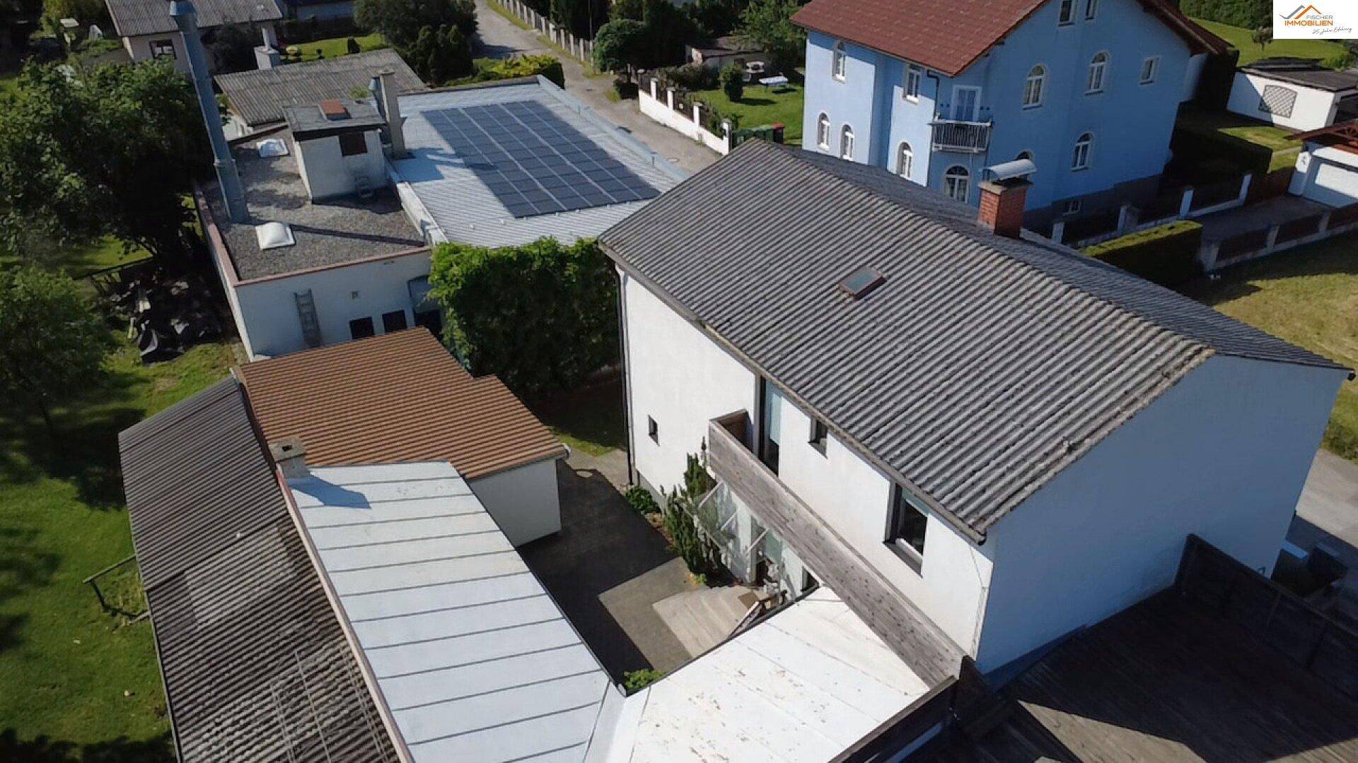 Luftaufnahme des Hauses von der Rückseite, mit dunklem Dach, kleinem Balkon und weiteren Gebäuden in der Nachbarschaft.