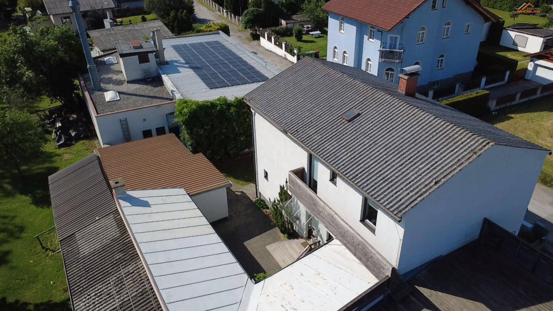 Luftaufnahme der Rückseite des Hauses mit kleinem Balkon und grauem Ziegeldach, umgeben von Grünflächen.