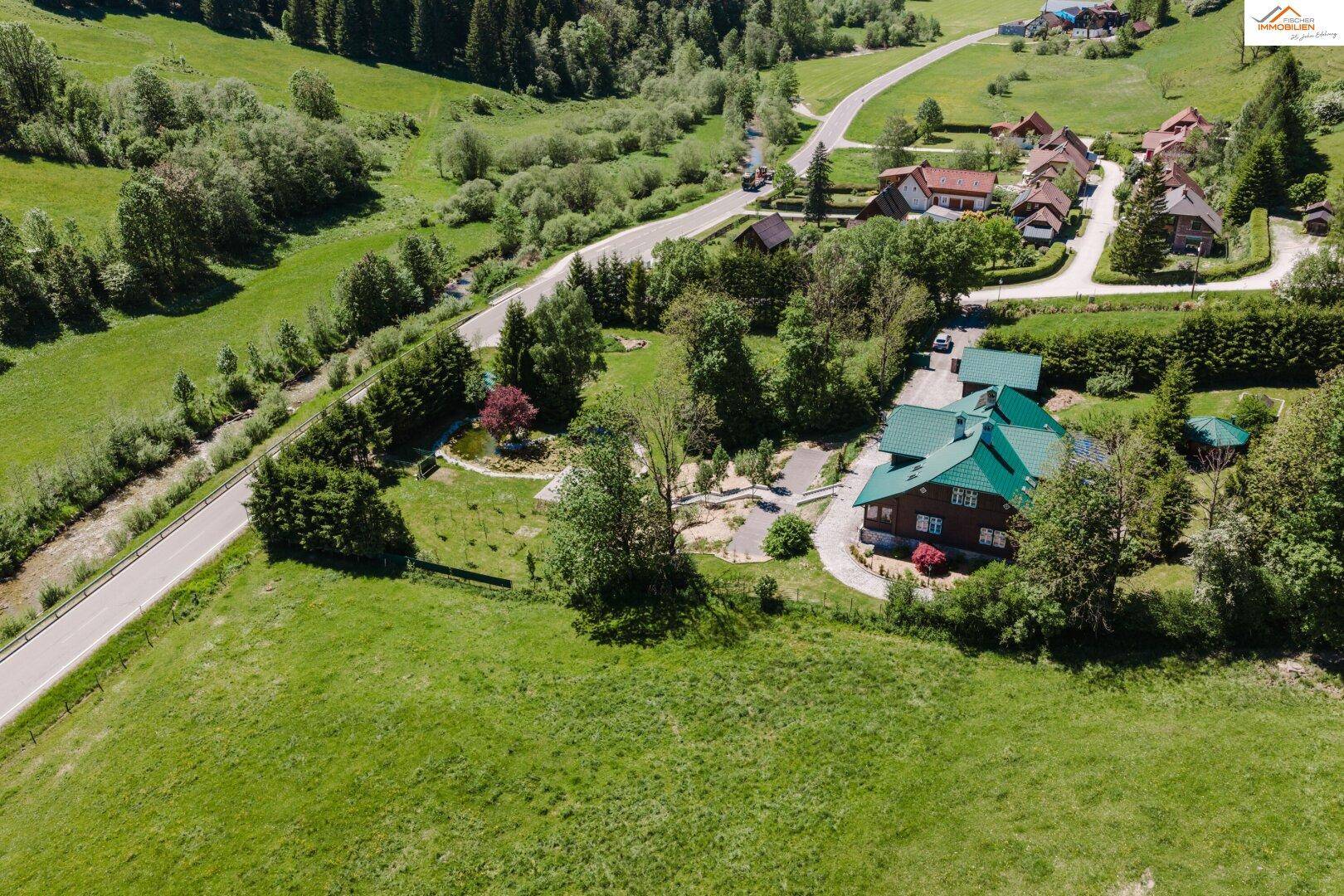 Weitläufige Luftaufnahme des Anwesens mit Haus, Garten und angrenzender Straße in ländlicher Umgebung.