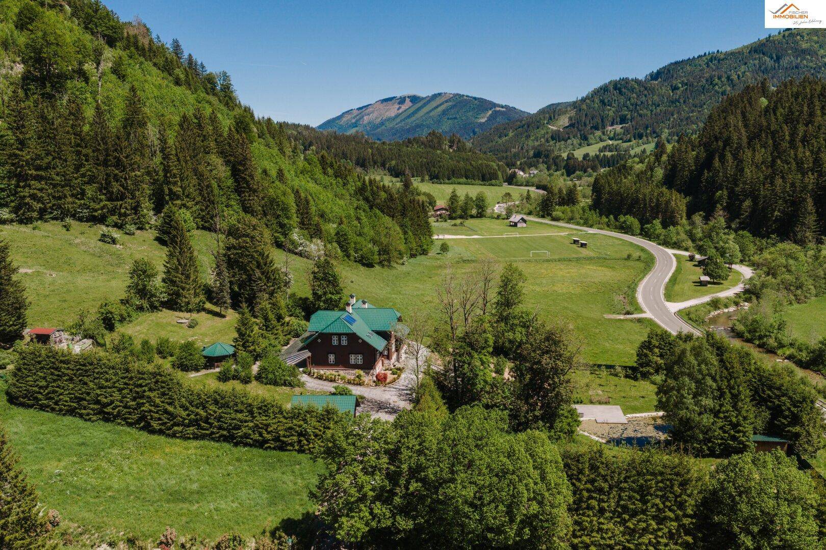 Panoramablick auf das Anwesen in einem grünen Tal, umgeben von bewaldeten Bergen und einer malerischen Landschaft.