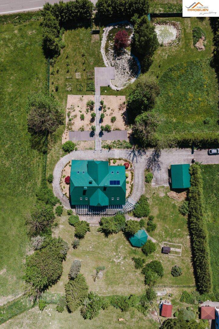 Vogelperspektive des Hauses mit grünem Dach, Solaranlage und gepflegtem Gartenbereich mit Wegen.
