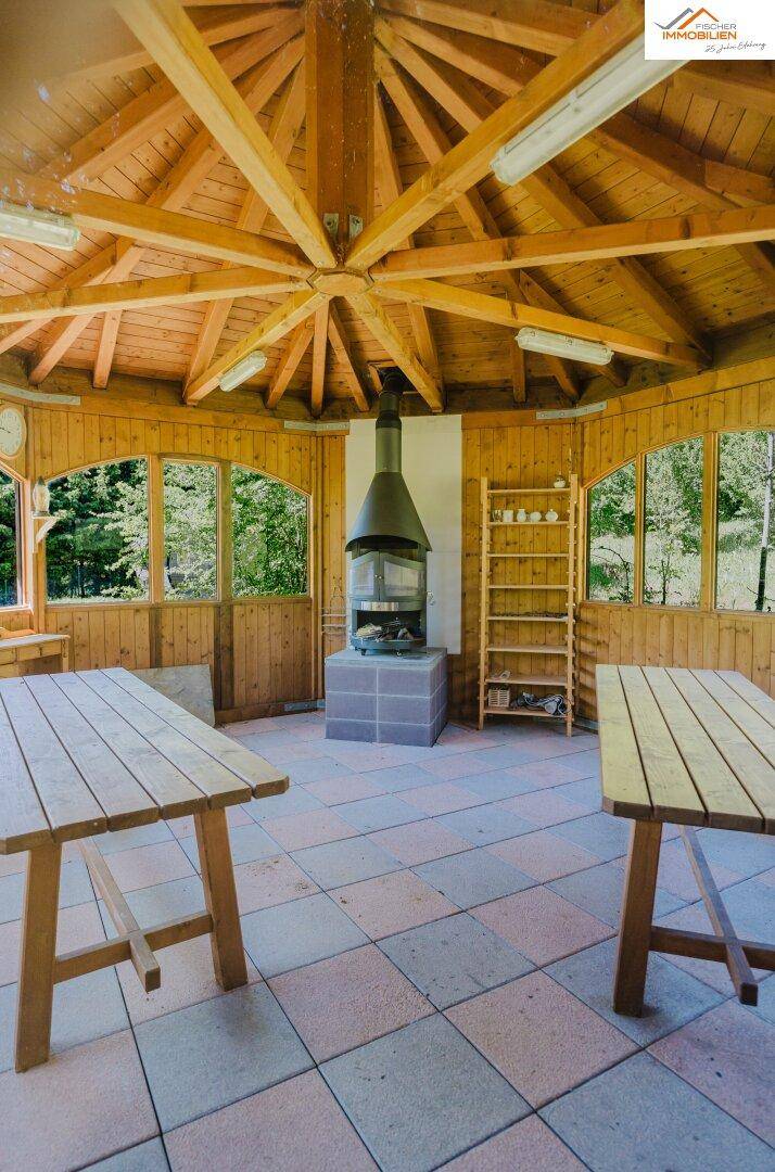 Gemütlicher Holzpavillon mit Kaminofen, Holztischen und Blick ins Grüne, ideal für gesellige Stunden.