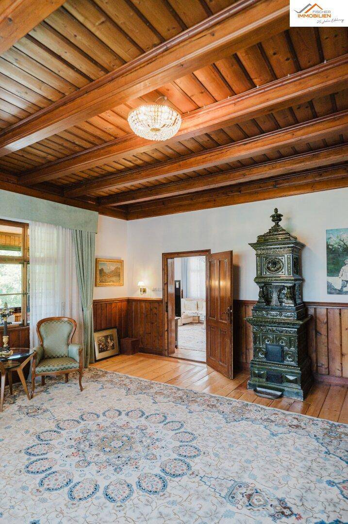 Traditionelles Wohnzimmer mit Holzbalkendecke, Kachelofen, gemustertem Teppich und klassischer Einrichtung.