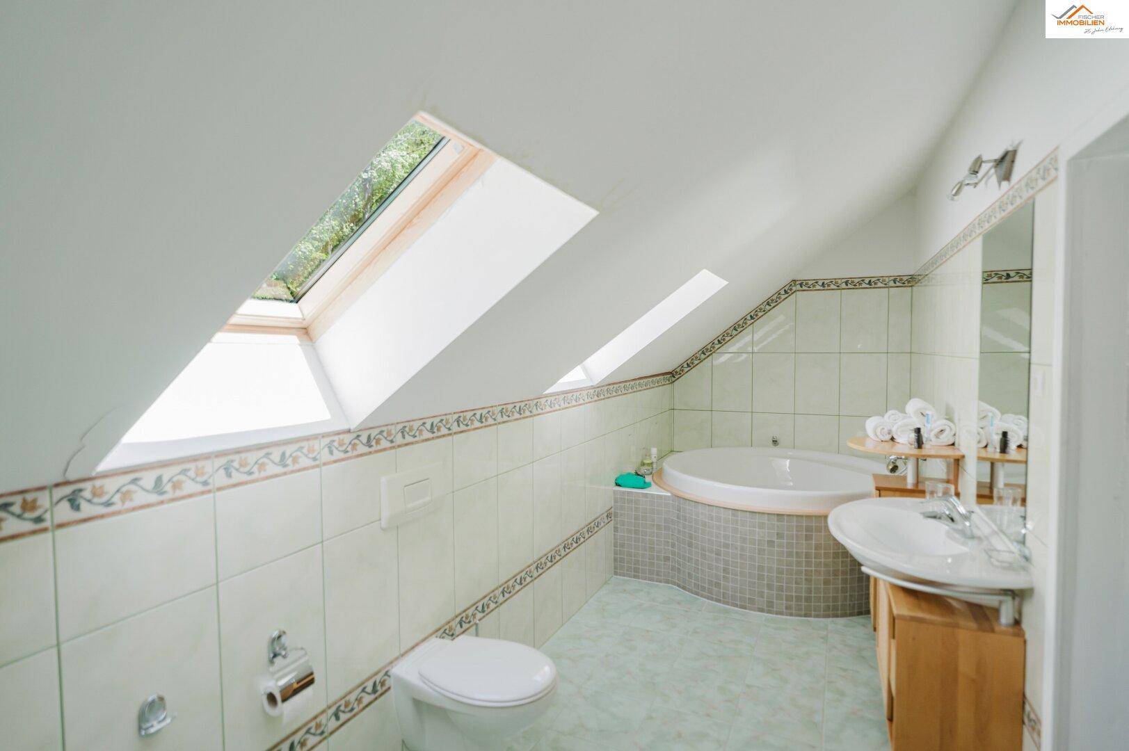 Helles Badezimmer mit Eckbadewanne, Waschbecken, Toilette und Dachfenstern für natürliches Licht.