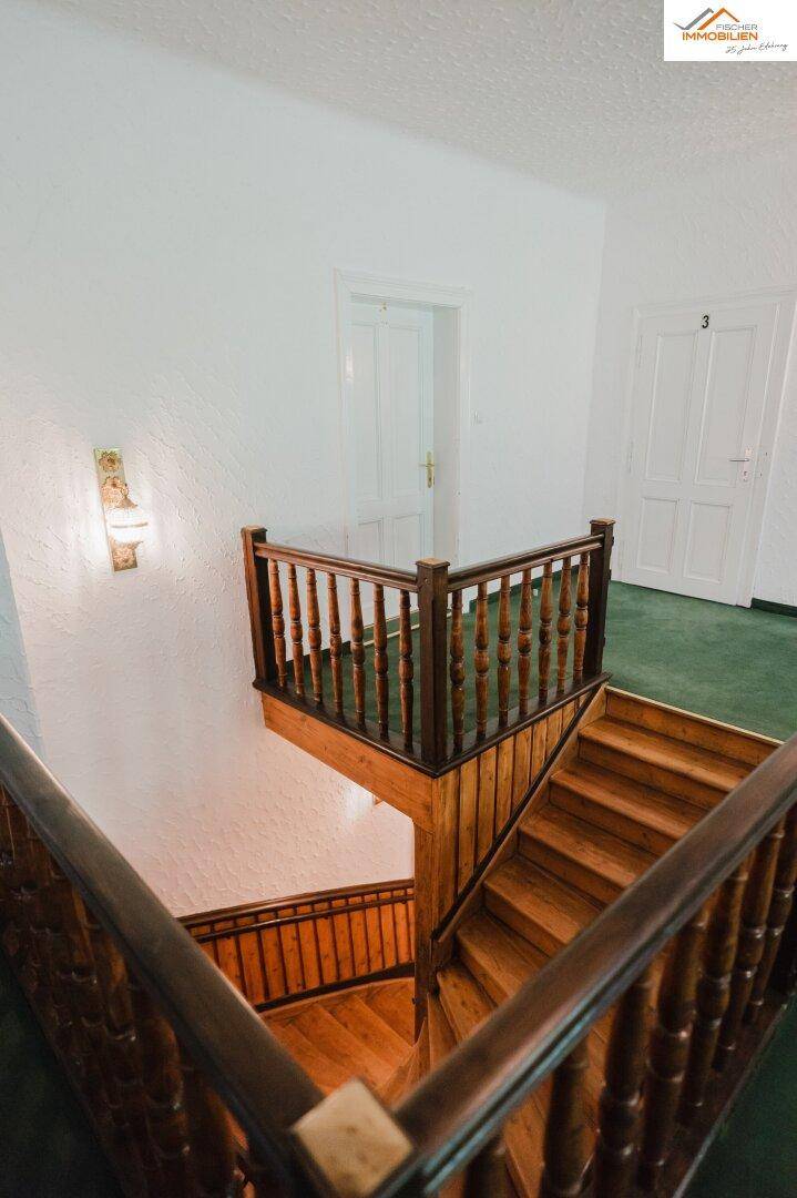 Elegantes Holztreppenhaus mit grünen Teppichstufen und traditionellem Geländer, das die Etagen verbindet.