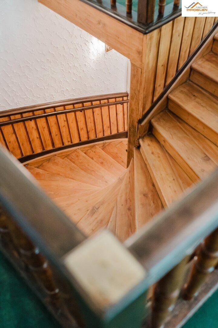 Hölzerne Wendeltreppe mit traditionellem Geländer, die verschiedene Etagen in einem charmanten Gebäude verbindet.