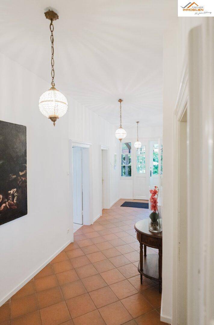 Heller Flur mit Terrakotta-Fliesenboden, weißen Wänden und dekorativen Hängelampen, mit Zugang nach draußen.