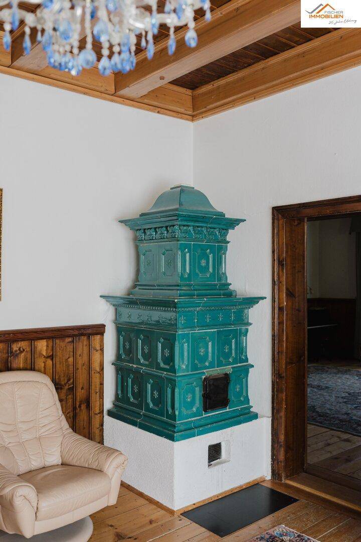 Detailansicht eines grünen Kachelofens in einem Raum mit Holzvertäfelung und hellem Sessel.