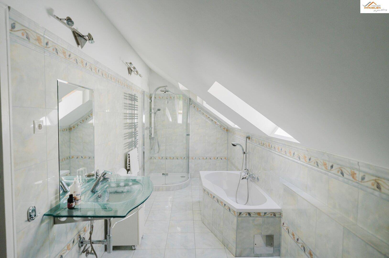 Helles Badezimmer im Dachgeschoss mit Badewanne, Duschkabine, modernem Glaswaschbecken und Dachfenstern.