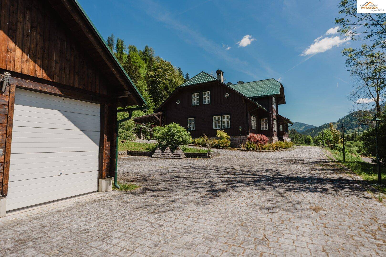 Außenansicht mit separater Garage und Haupthaus, verbunden durch eine gepflasterte Auffahrt in ländlicher Umgebung.