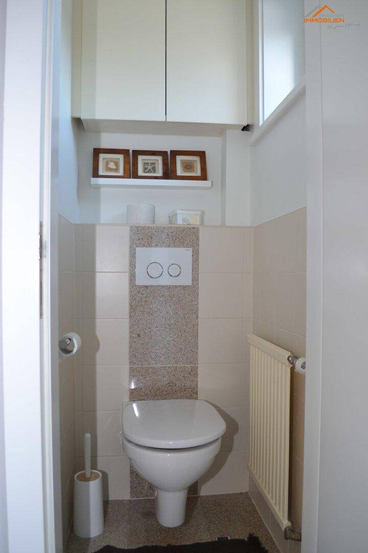 Kleines Gäste-WC mit beigefarbenen Fliesen, wandhängendem WC und Heizkörper.