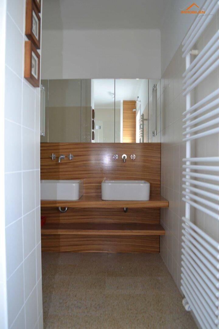 Modernes Badezimmer mit Doppelwaschbecken, Holzverkleidung und beheiztem Handtuchhalter.