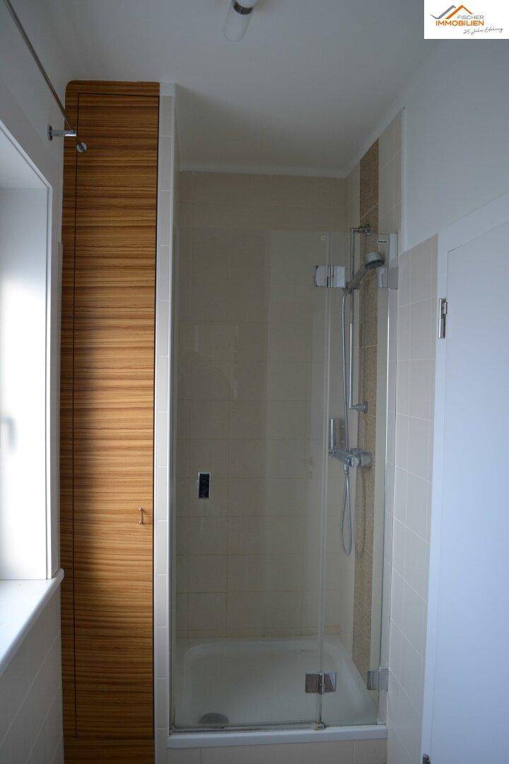 Duschbad mit Glasduschkabine, beigefarbenen Fliesen und Holzverkleidung.