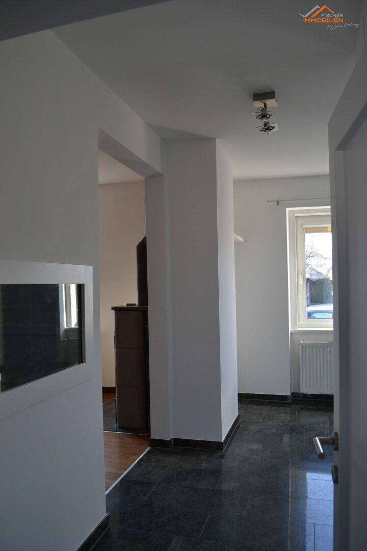 Moderner Flur mit dunklem Fliesenboden, weißen Wänden und natürlichem Lichteinfall durch ein Fenster.