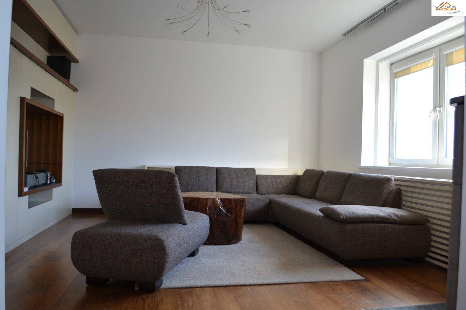 Gemütliches Wohnzimmer mit großem Sofa, Holzboden und viel Tageslicht.