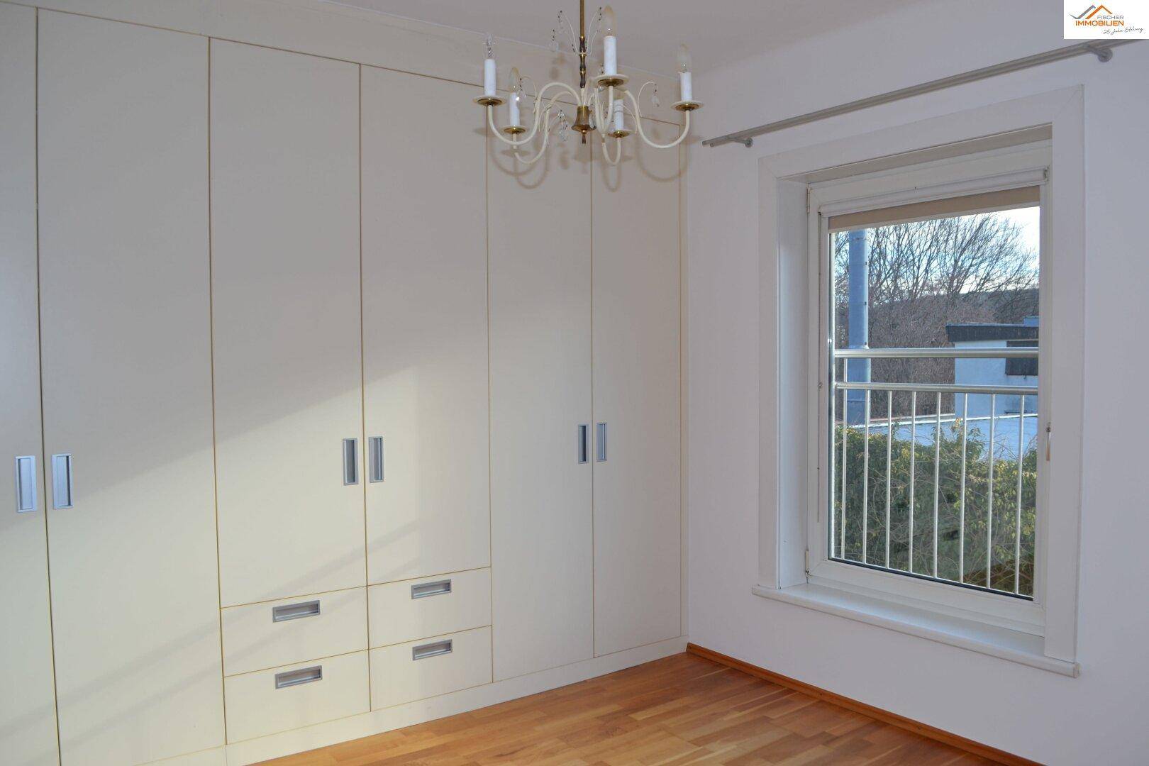 Schlafzimmer mit Einbauschränken, Holzboden und großem Fenster.