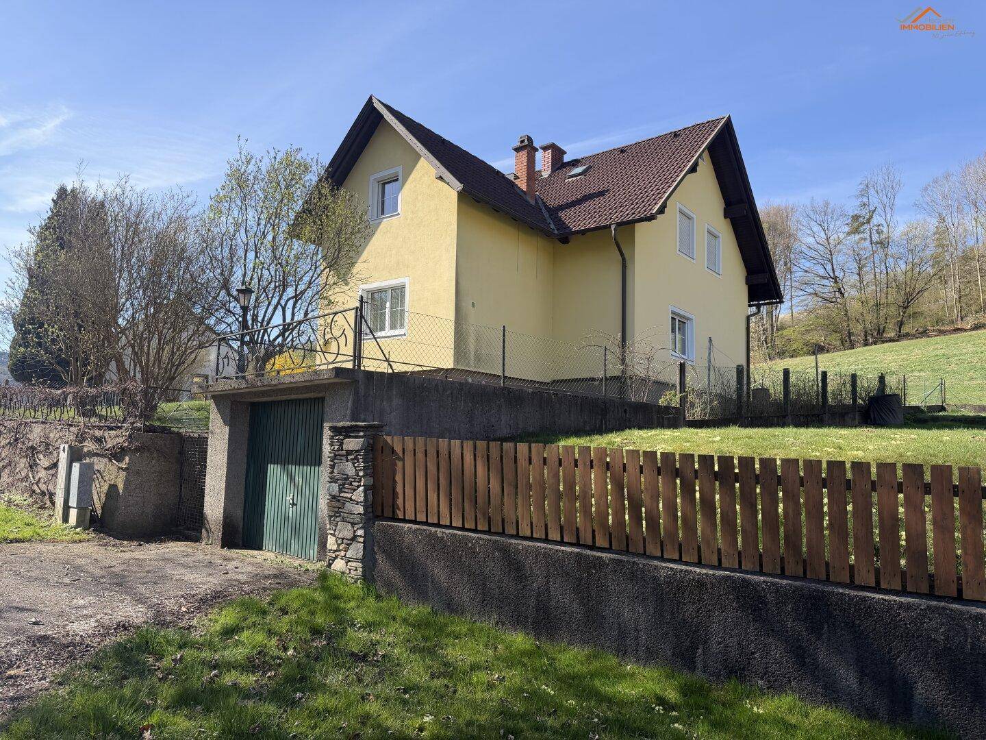 Einfamilienhaus mit integrierter Garage und Holzzaun in ländlicher Umgebung.