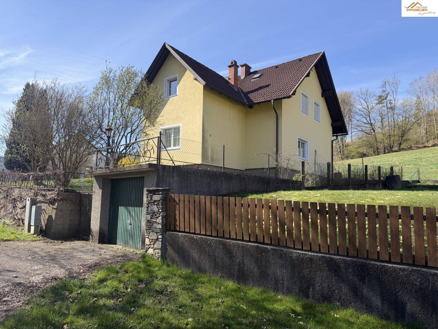 Seitenansicht des Hauses mit integrierter Garage und umzäuntem Gartenbereich am Hang.