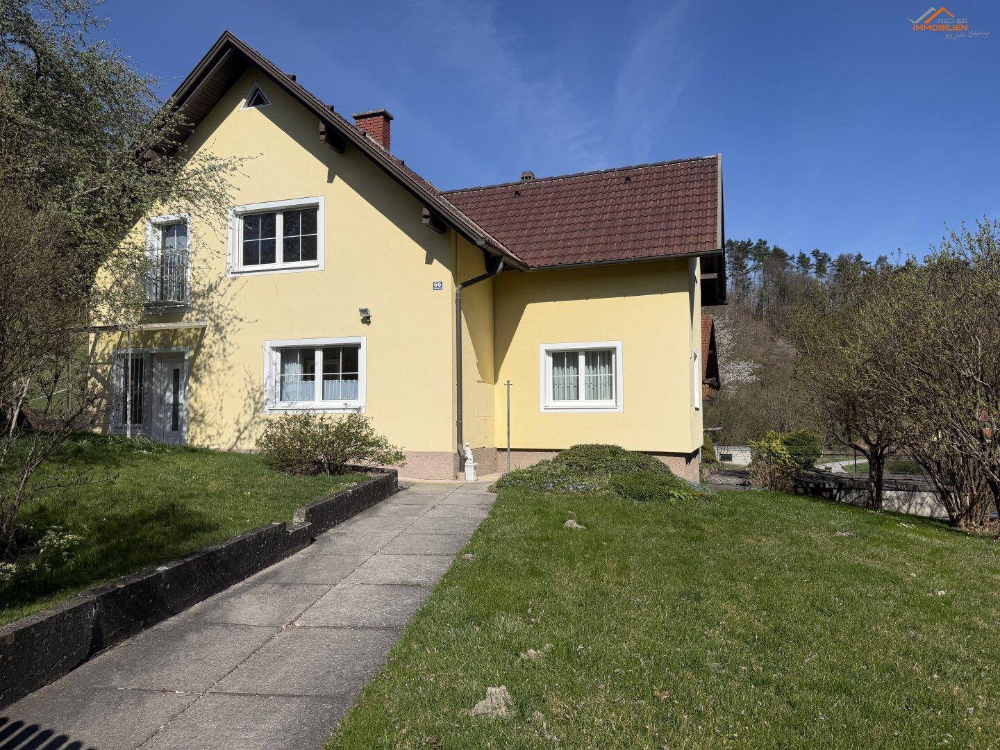 Seitenansicht des gelben Einfamilienhauses mit Garten und sonnigem Wetter.
