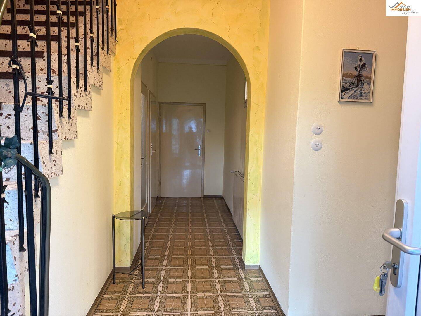Eingangsbereich mit gemustertem Fliesenboden und geschwungener Treppe zum Obergeschoss.