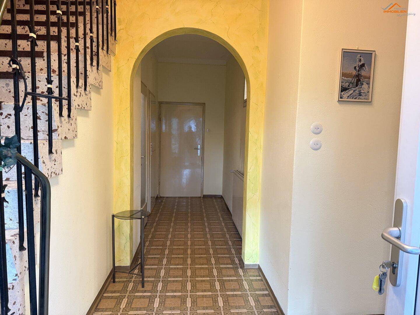 Eingangsbereich mit Terrazzoboden, Bogendurchgang und Treppe zum Obergeschoss.