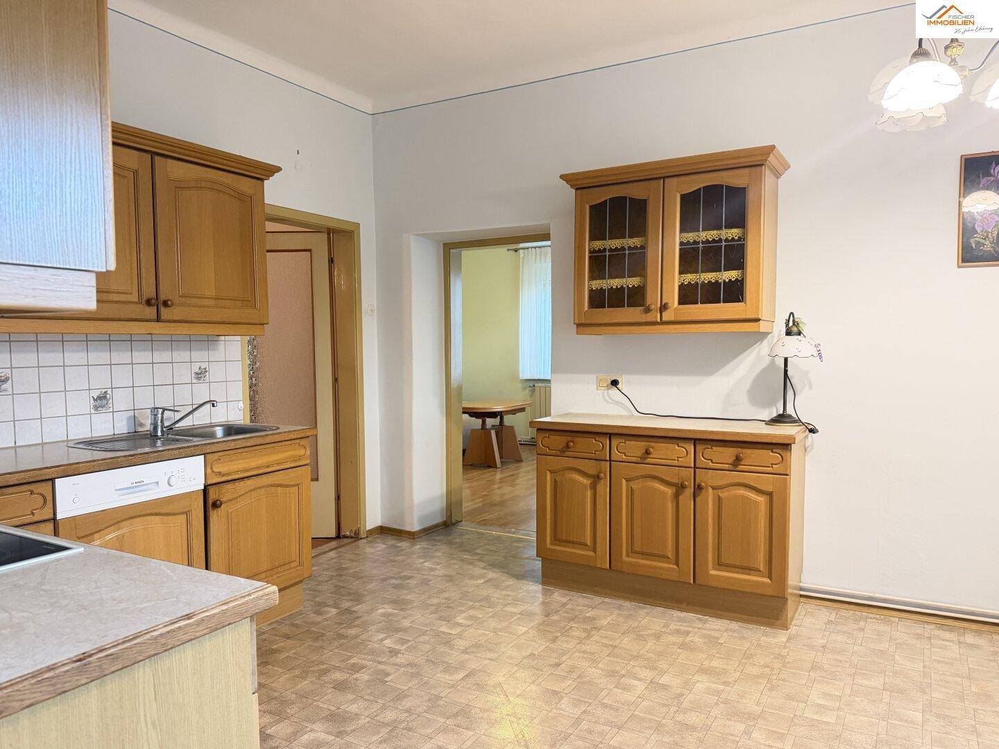 Traditionelle Küche mit Holzschränken, Fliesenrückwand und Blick in einen weiteren Raum.