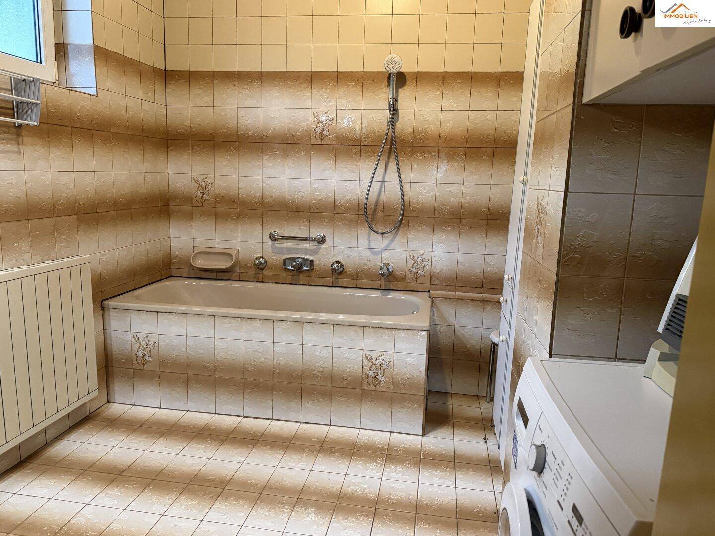 Badezimmer mit Badewanne, beigen Fliesen und Waschmaschine, in gutem Zustand.
