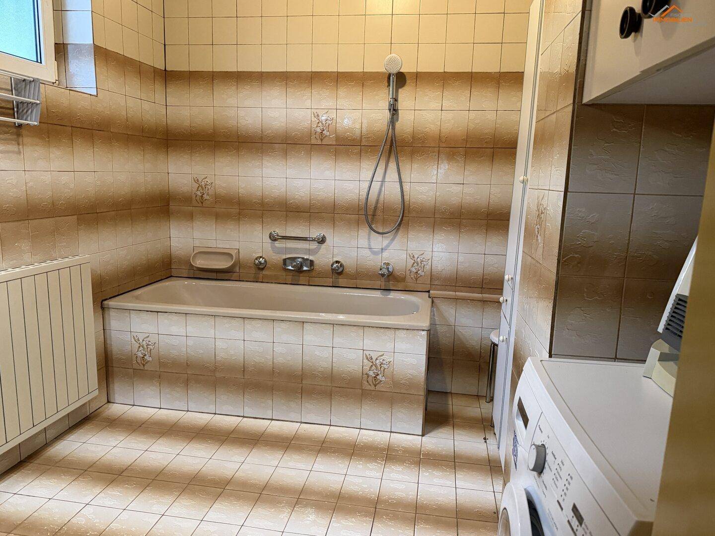 Badezimmer mit Badewanne, Fliesen in Brauntönen und Waschmaschine.