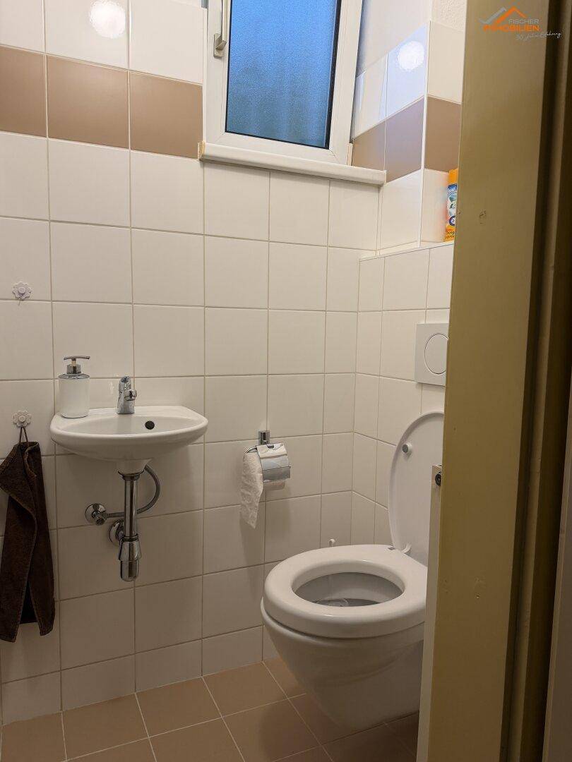 Kleines Gäste-WC mit Waschbecken, Toilette und Fenster.