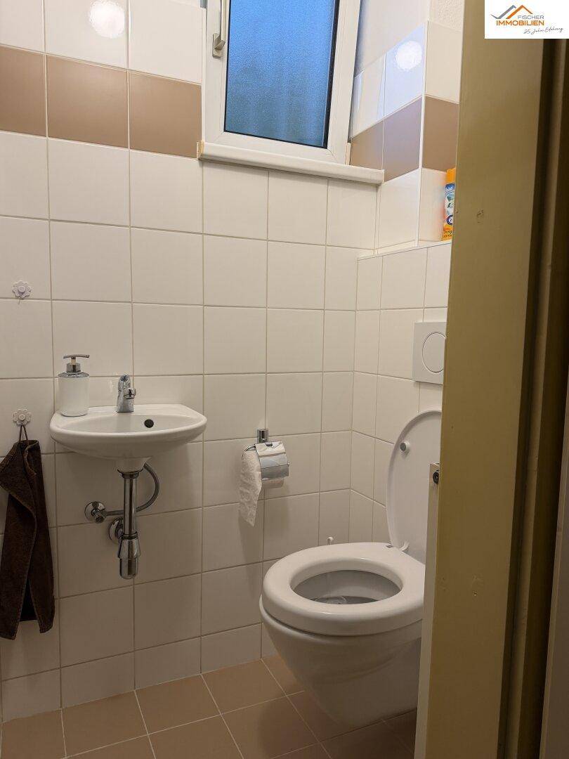 Kleines Gäste-WC mit Waschbecken, Toilette und Fenster, hell gefliest.