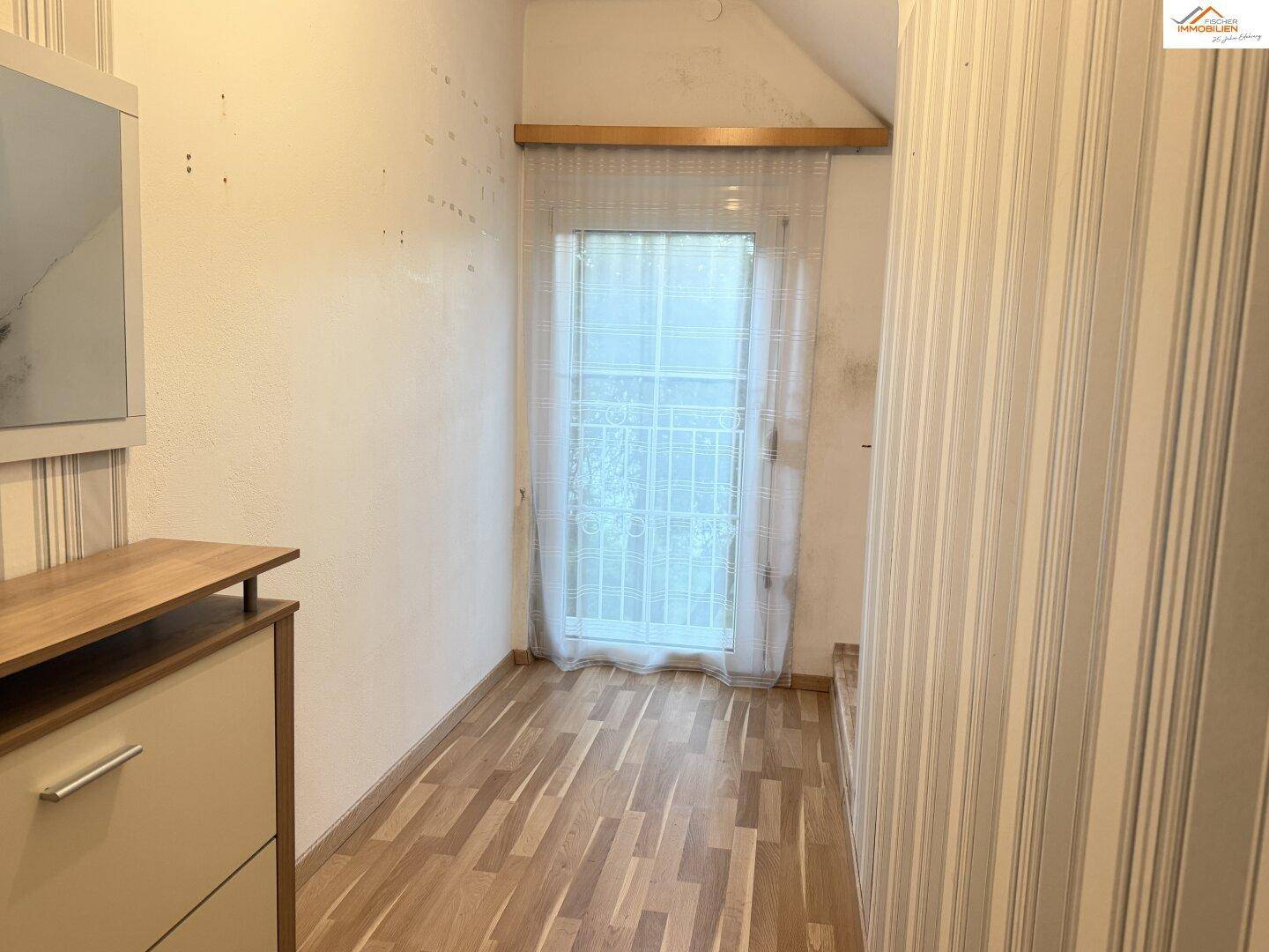 Kleiner Raum mit Laminatboden, gestreifter Tapete und Fenster, renovierungsbedürftig.