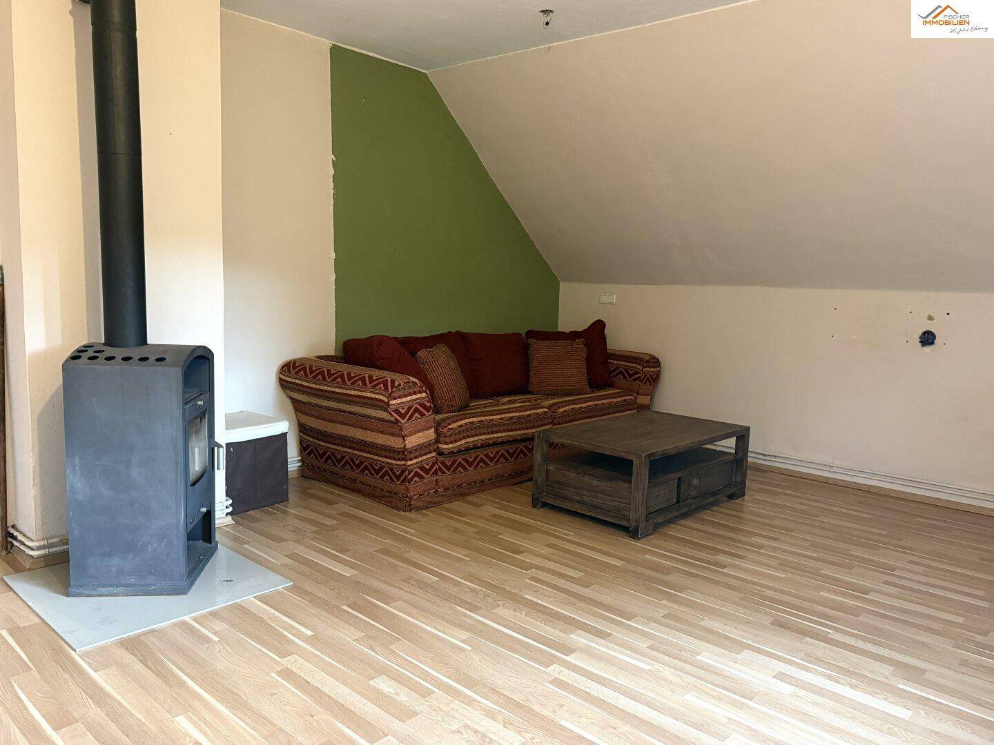 Gemütliches Wohnzimmer im Dachgeschoss mit Kaminofen, Sofa und Laminatboden.