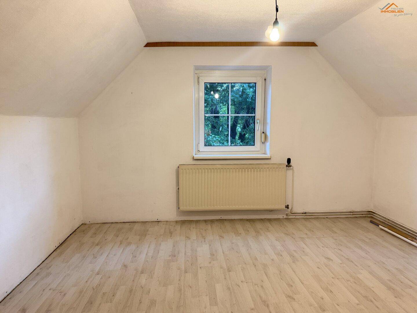 Helles Dachzimmer mit Laminatboden, Fenster und schrägen Decken.