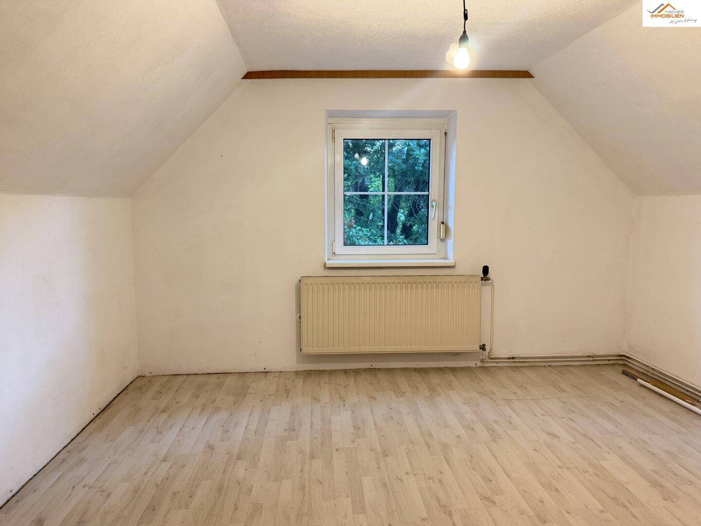 Dachgeschossraum mit Laminatboden, Fenster und Heizkörper, bereit zur individuellen Gestaltung.
