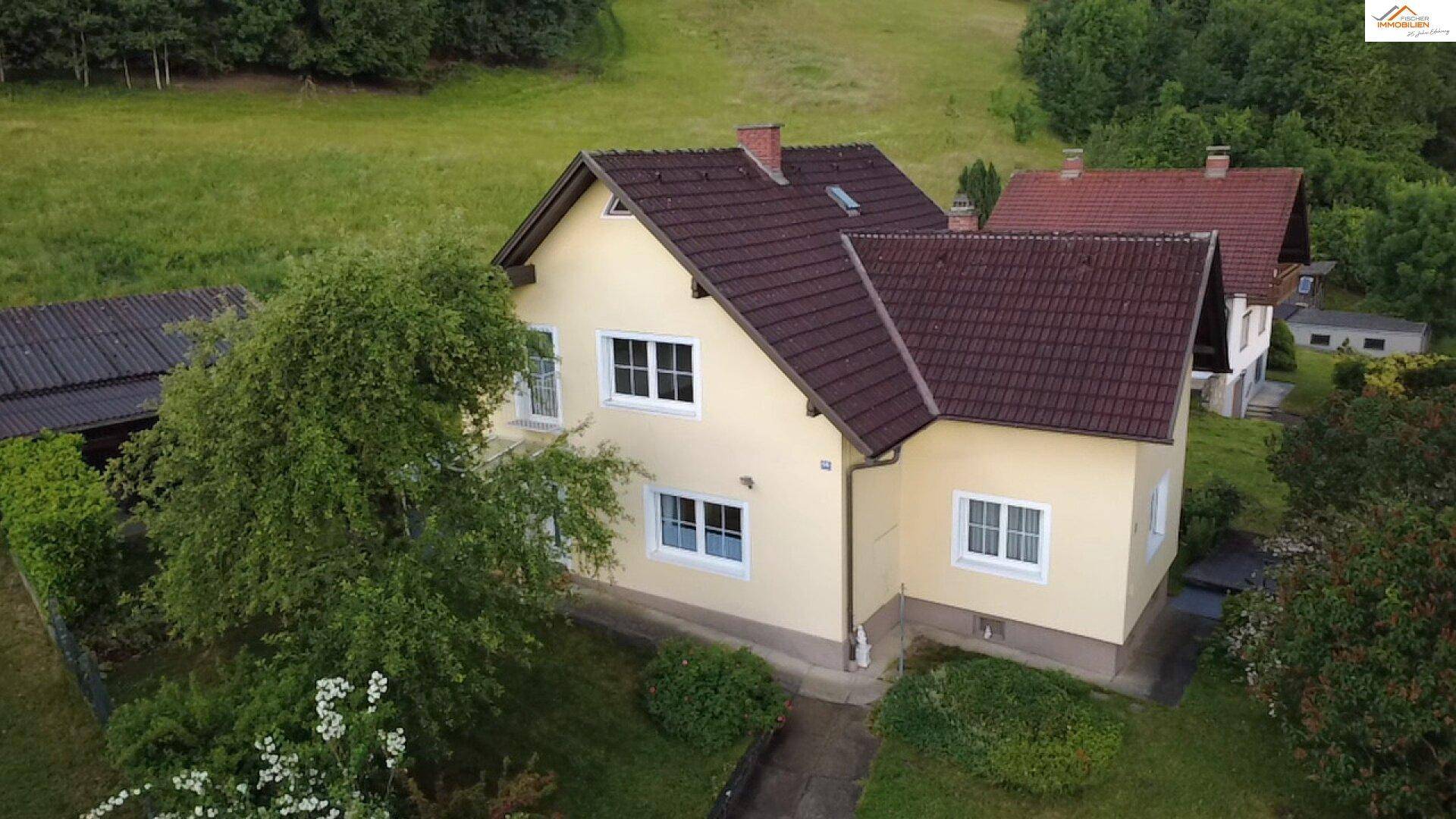 Luftaufnahme des gelben Hauses mit angrenzendem Carport und weiten Grünflächen.