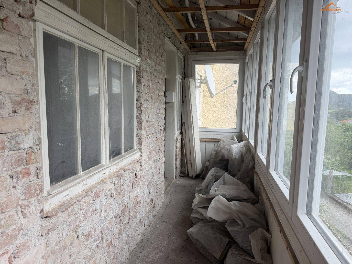 Geschlossene Loggia im Rohzustand mit unverputzten Ziegelwänden und vielen Fenstern.