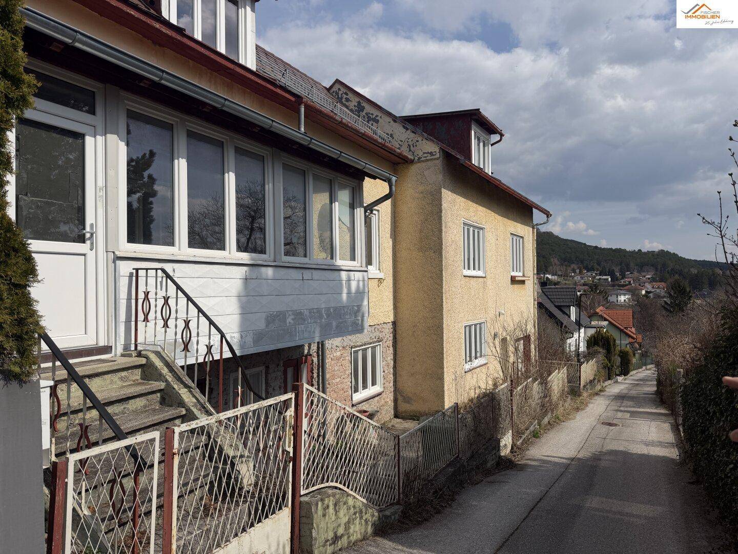Altes Gebäude mit gelber Fassade und Außentreppe an einer leicht ansteigenden Straße.