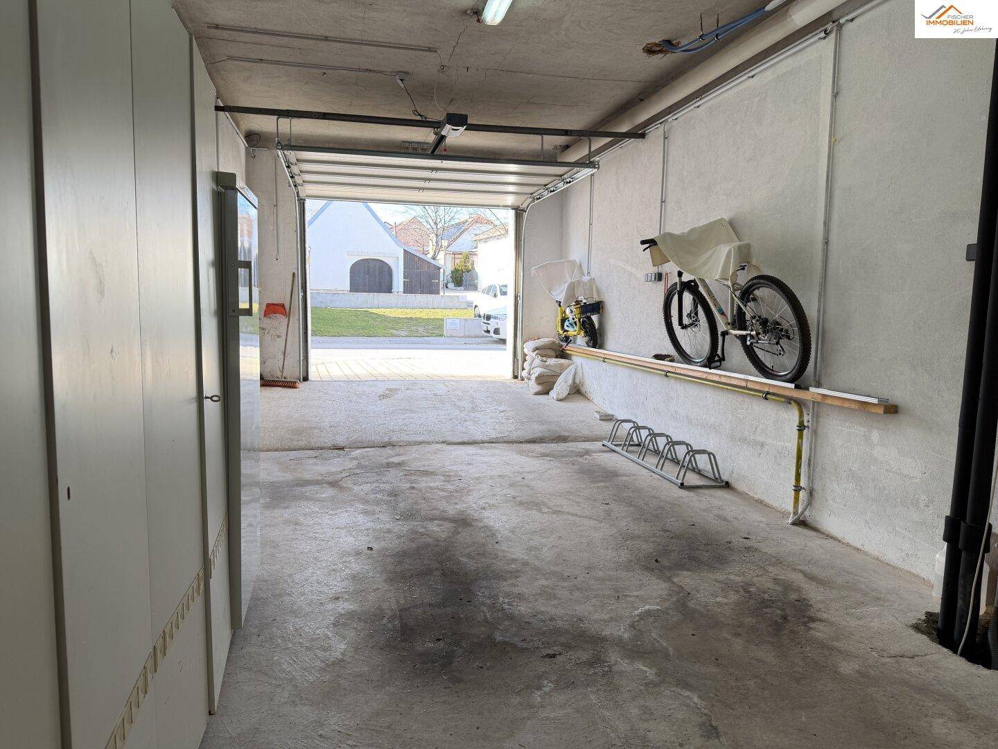 Geräumige Garage mit Betonboden, Stauraum und offenem Garagentor zur Straße, bietet Platz für Fahrzeuge und Fahrräder.