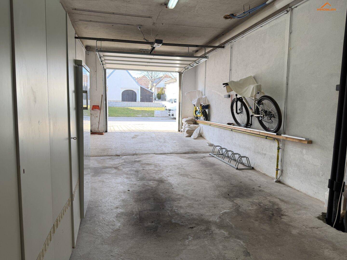 Geräumige Garage mit Betonboden, offenem Garagentor und Abstellmöglichkeiten.