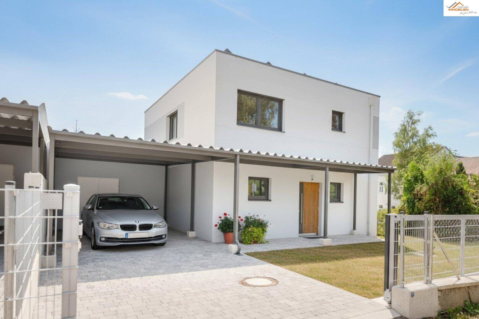 Modernes Einfamilienhaus mit Carport und gepflegtem Vorgarten unter blauem Himmel.