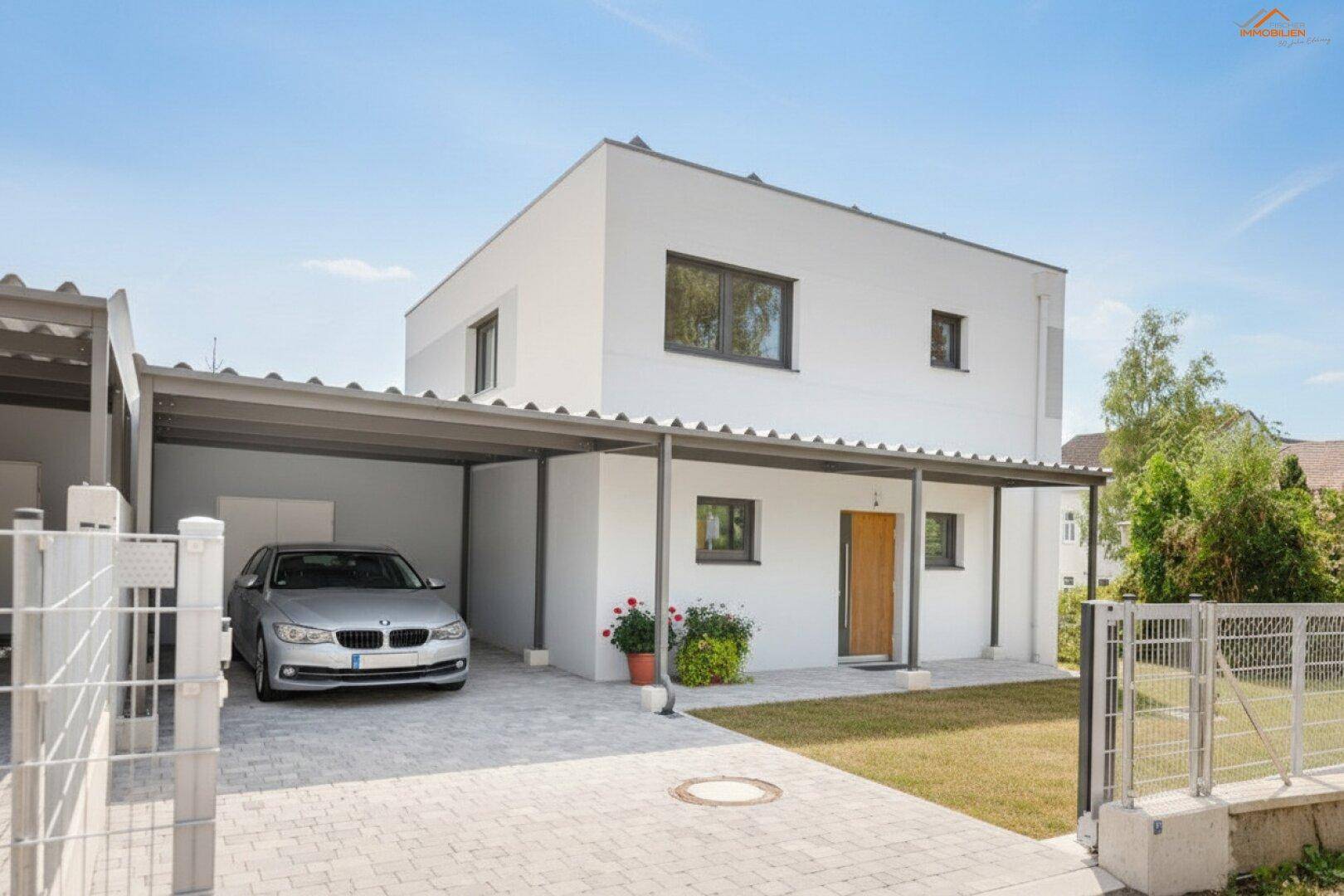 Modernes weißes Einfamilienhaus mit Carport, gepflasterter Auffahrt und kleinem Vorgarten.